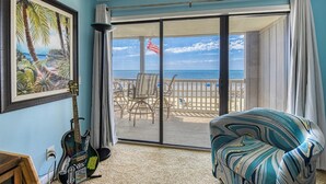 A room with a view of a beach, a guitar, and a patterned armchair.