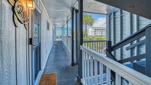 A covered corridor with a wooden floor, a railing on one side, and a view of buildings in the distance.