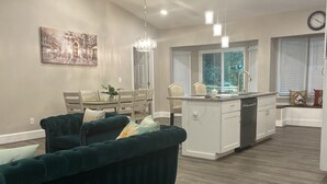 A modern kitchen with white cabinets, a dining area with a green sofa, and a dining table.
