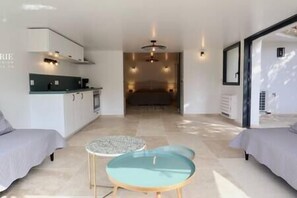 Quarto moderno e bem iluminado com cozinha compacta, área de refeições com mesa redonda e uma cama ao fundo.
