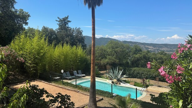Una piscina con sillas de descanso, rodeada de vegetación y vistas a colinas distantes.
