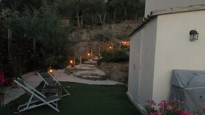 Un jardín con césped artificial, un cobertizo blanco y un muro de piedra.