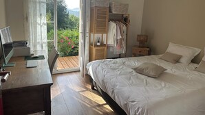 Un dormitorio con cama, escritorio con ordenador, armario y vistas a la vegetación exterior.
