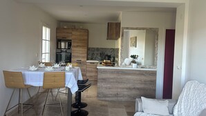 Un comedor con una mesa dispuesta para cuatro, una cocina al fondo y una sala de estar con un sofá.