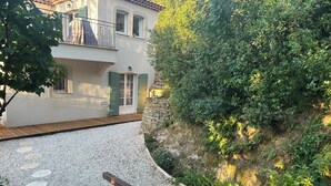 Una casa de dos pisos con un balcón, una terraza de madera y un camino de grava que conduce a la entrada.