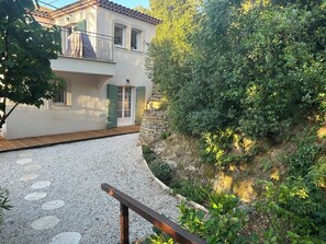 Ein zweistöckiges Haus mit einem Balkon, einer Holzterrasse und einem Kiesweg, der zum Eingang führt.