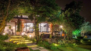 A traditional-style building with a well-lit entrance, stone steps, and lush greenery. - The Forest Museum (Zhuolan)