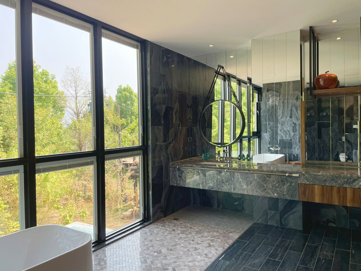 Un baño moderno con ventanas amplias, un tocador de mármol y vistas a zonas verdes.