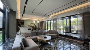 A modern living room with a sectional sofa, a round coffee table, and a kitchen area in the background. - The Forest Museum (Zhuolan)