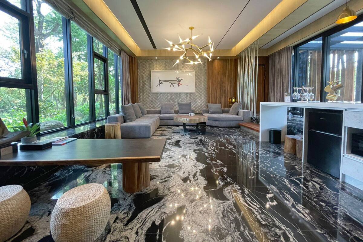 A modern living room with a large sectional sofa, a marble floor, and a dining area with a kitchen counter.