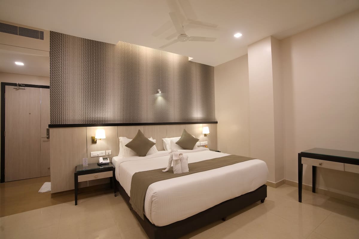 A hotel room with a large bed, two bedside tables, a desk, a ceiling fan, and a patterned wall.