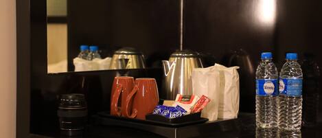 Um minibisco do hotel com cafeteira, duas canecas, água engarrafada e lanches.