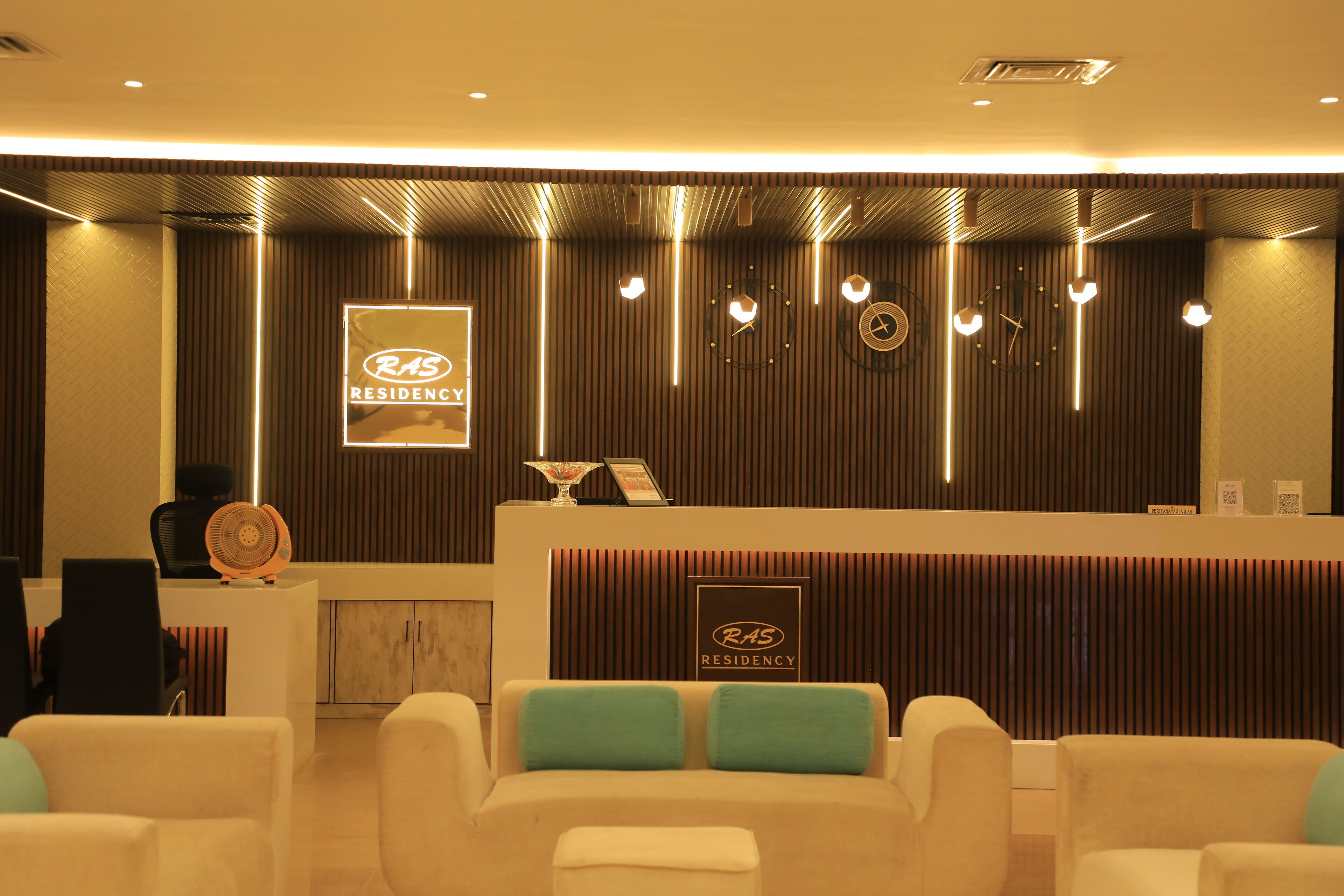A reception area with a reception desk, chairs, and a wall with vertical lines and a logo.