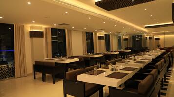 A modern dining area with long tables, chairs, and a high ceiling with recessed lighting.