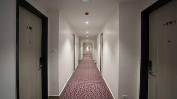 A hotel hallway with a patterned carpet, doors numbered 303 and 319, and a red emergency light on the ceiling.