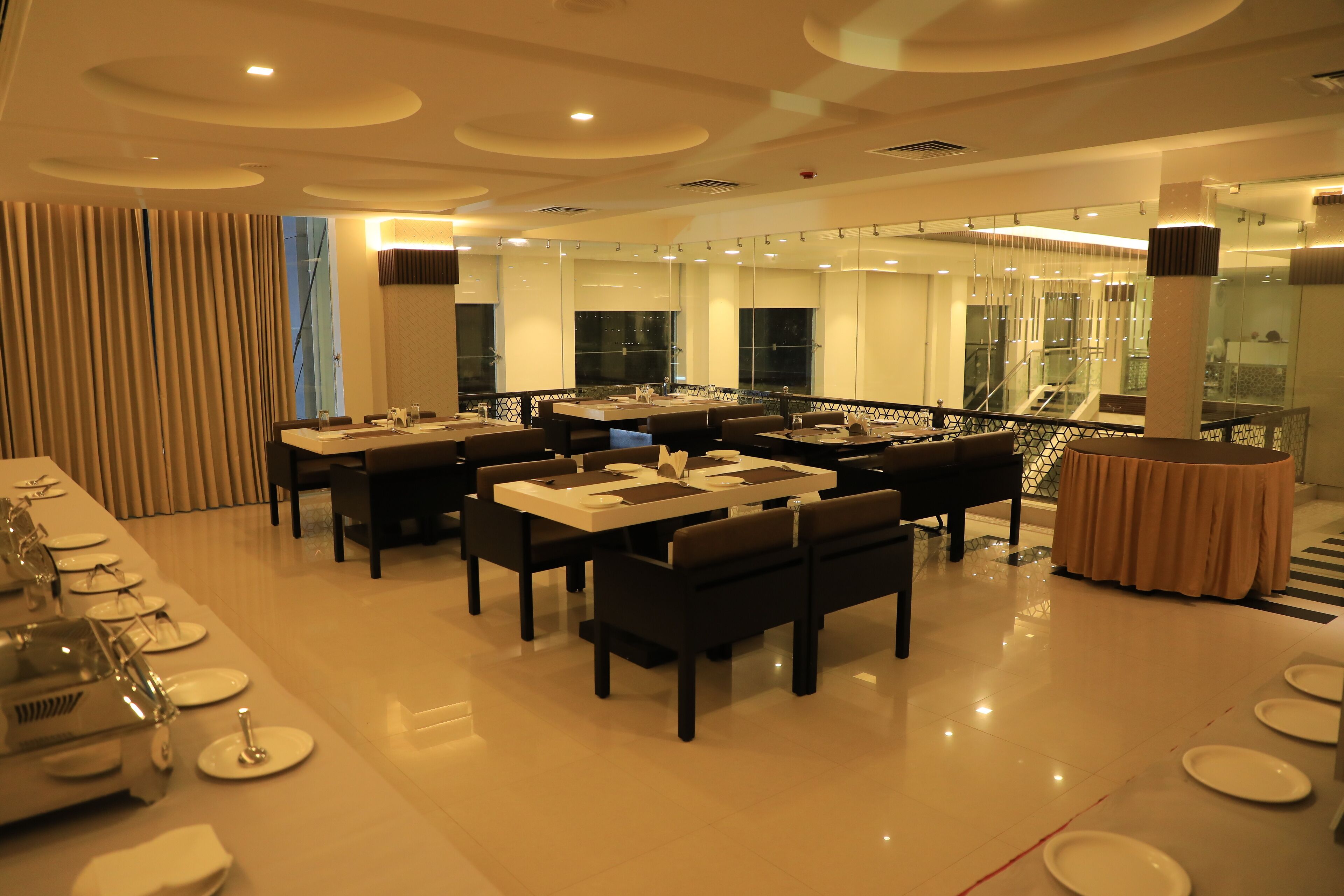 A modern dining area with multiple tables and chairs, a long counter with a sink, and a staircase leading to an upper level.