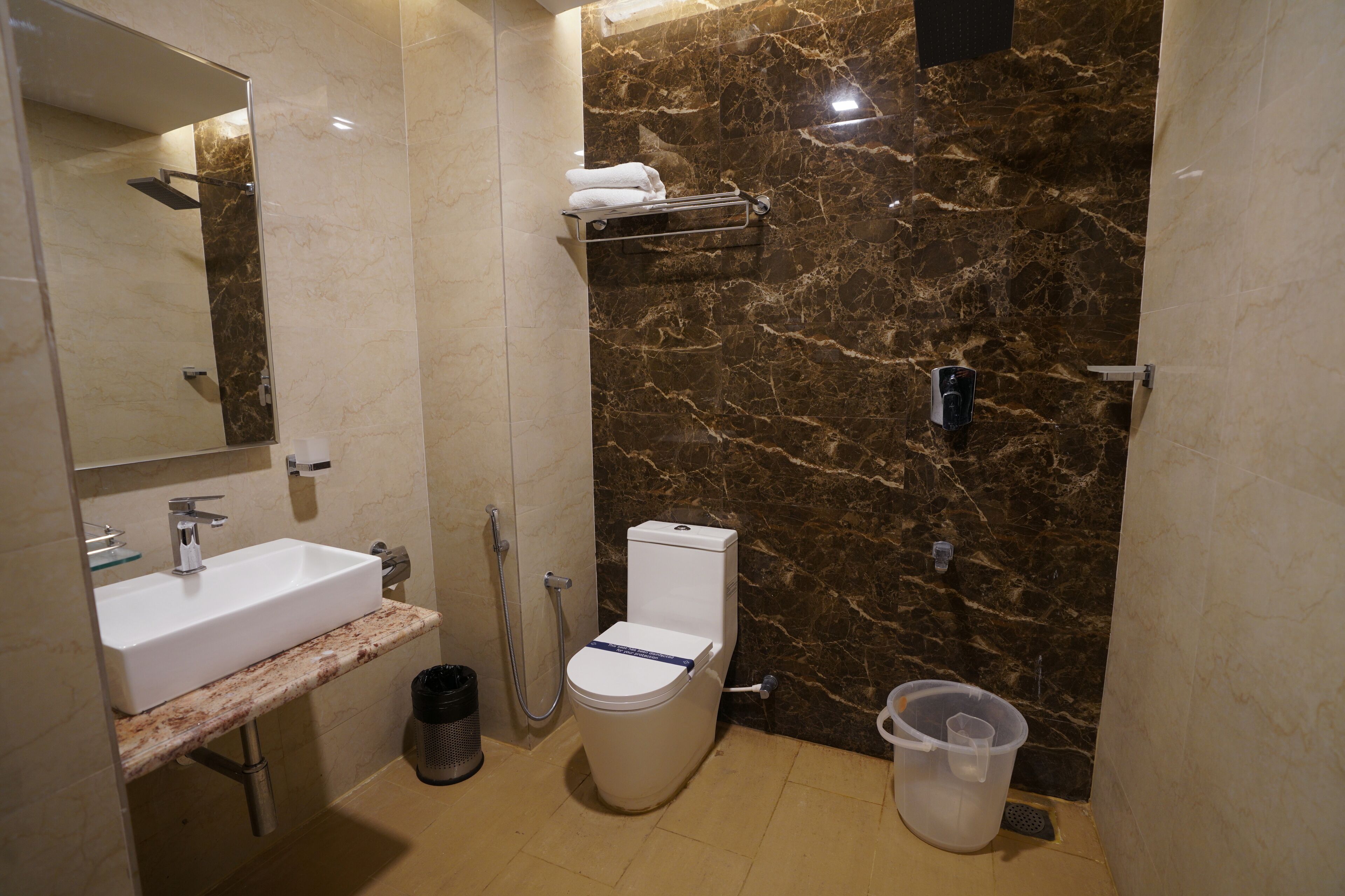 Un baño moderno con pared de mármol, un lavamanos blanco y un inodoro.