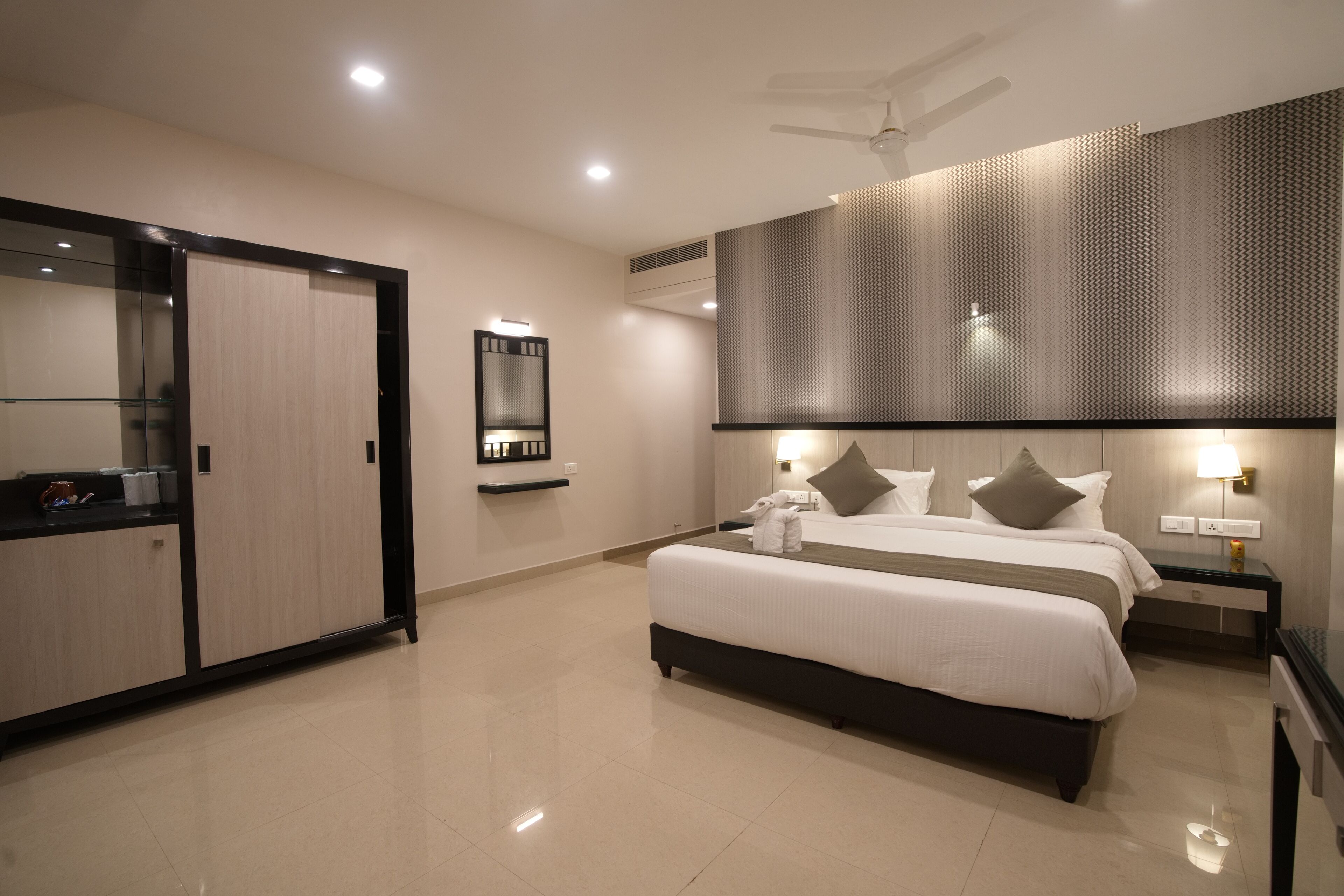 Una habitación de hotel moderna con una cama grande, una mesita de noche, un espejo, un armario y un ventilador de techo.
