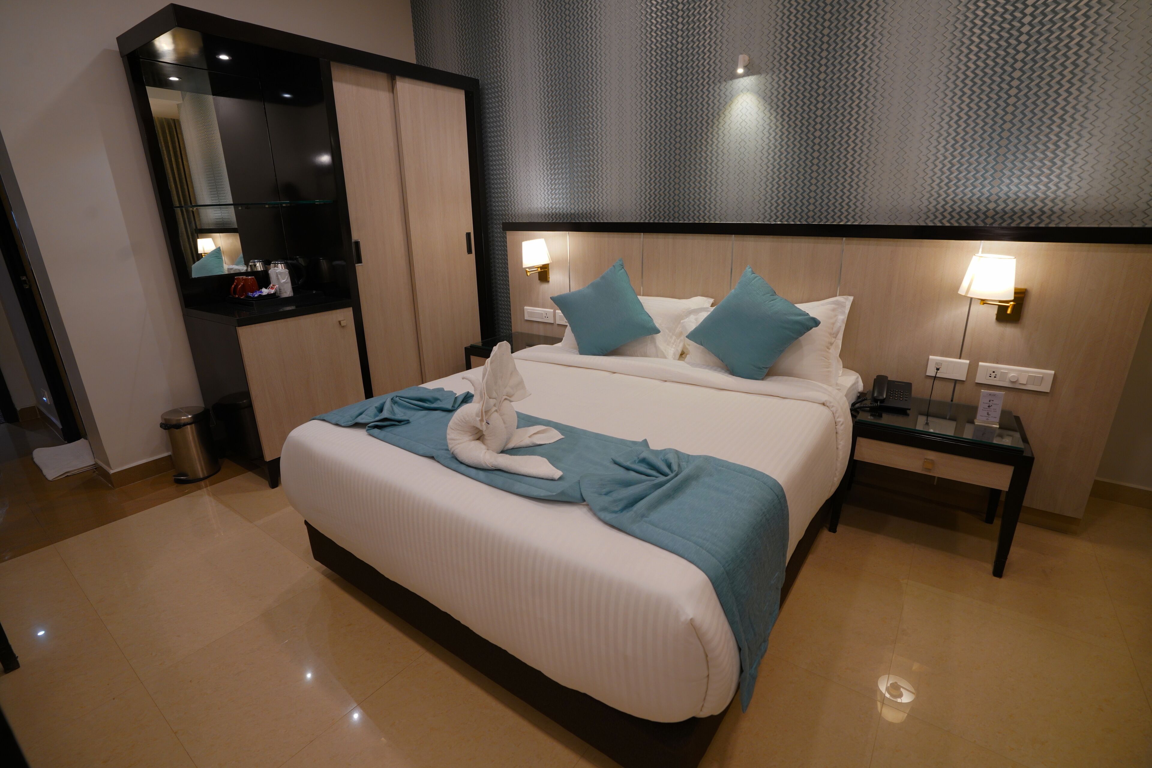 A modern hotel room with a large bed, two nightstands, a mirror, and a wardrobe.