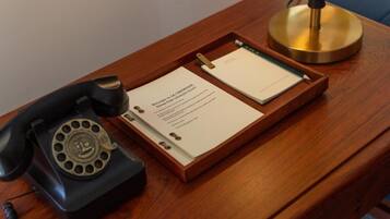 Escritorio de madera con un teléfono giratorio, una lámpara de escritorio de latón y un porta documentos con papeles.