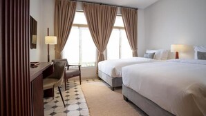 Habitación de hotel con dos camas, un escritorio, una silla y un ventanal con cortinas.