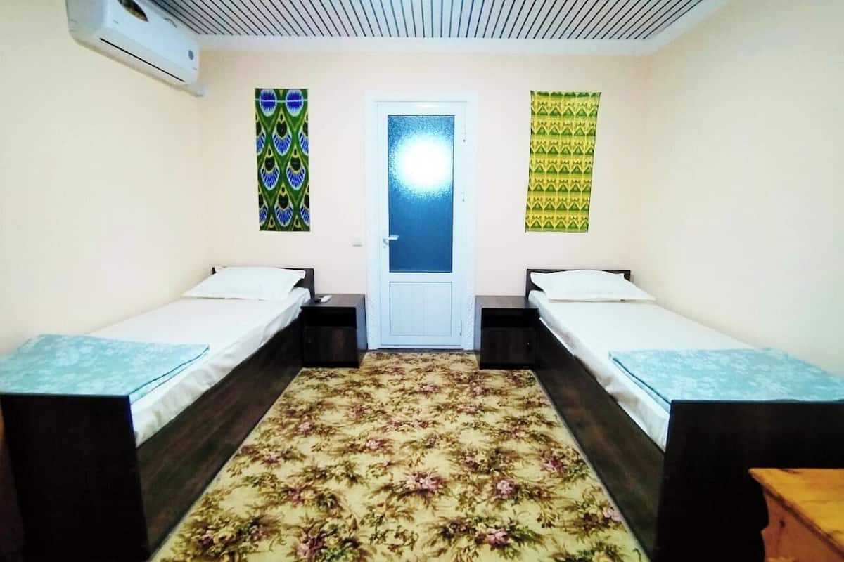 A room with two single beds, a floral carpet, a door with a frosted glass panel, and patterned curtains.