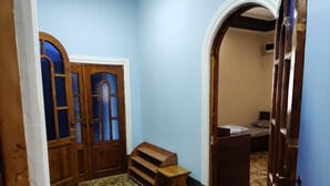 Una habitación con una puerta de madera, un banco y una cama al fondo.