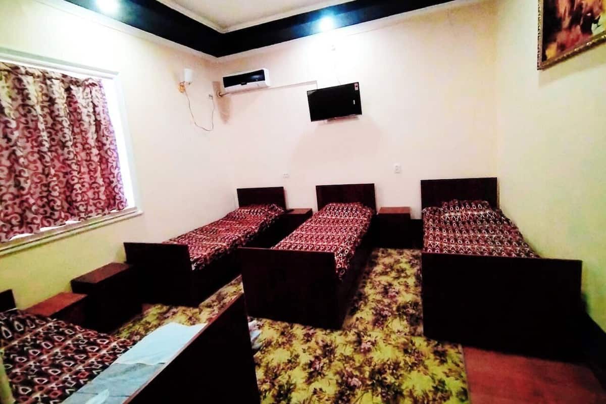 A room with four single beds, a window with patterned curtains, an air conditioning unit, and a mounted television.