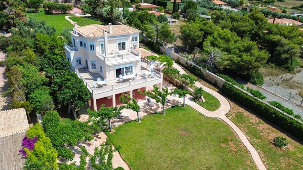 A two-story house with a balcony, surrounded by greenery and a paved driveway.