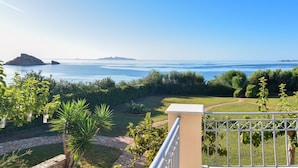 Un balcon avec vue sur la mer, un chemin pavé et un aménagement paysager verdoyant.