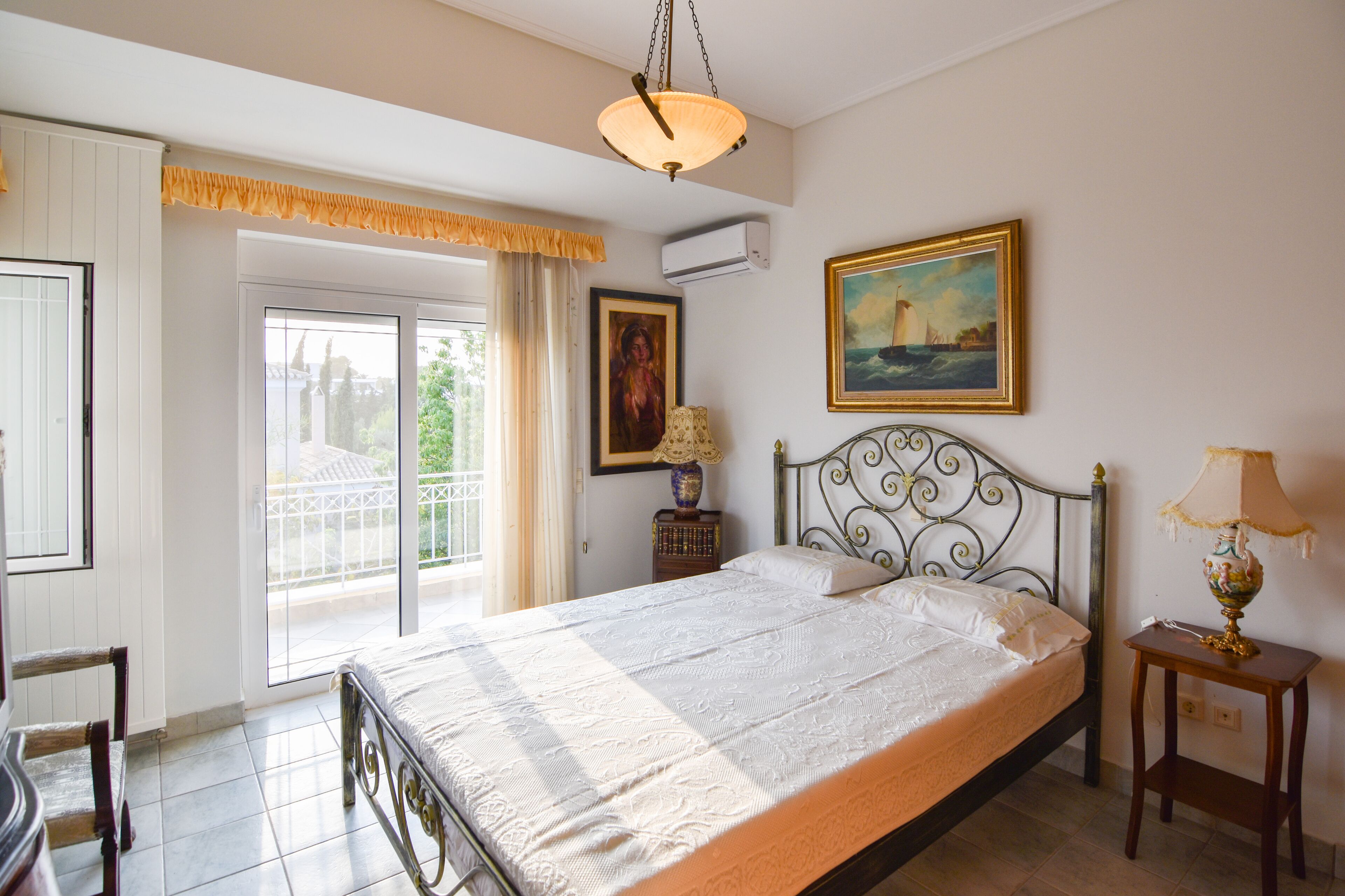 A bedroom with a bed, a nightstand, a lamp, a painting, and a window with curtains.