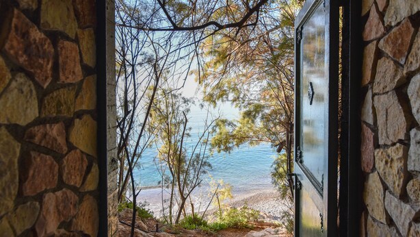 Un mur de pierre mène à une plage d’où l’on a une vue dégagée sur l’eau et les arbres.