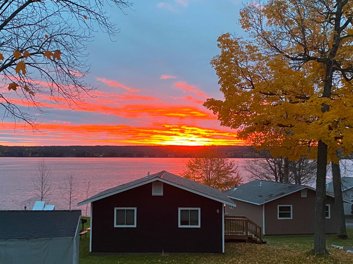 A lakeside view with two cabins and a sunset.