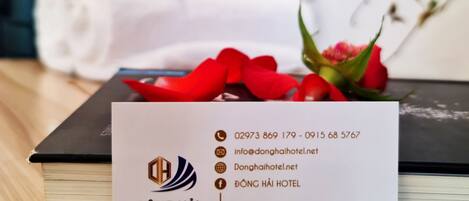 A hotel business card with contact information and the hotel's name, Dong Hai Hotel, placed on a wooden table with a book and a bouquet of red flowers.
