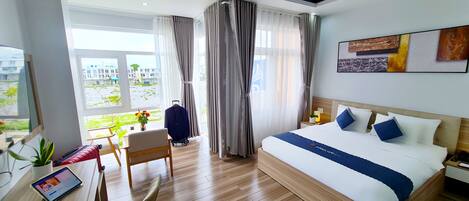 Habitación de hotel moderna con una cama grande, un escritorio con silla, una mesita con planta en maceta y vistas al exterior.