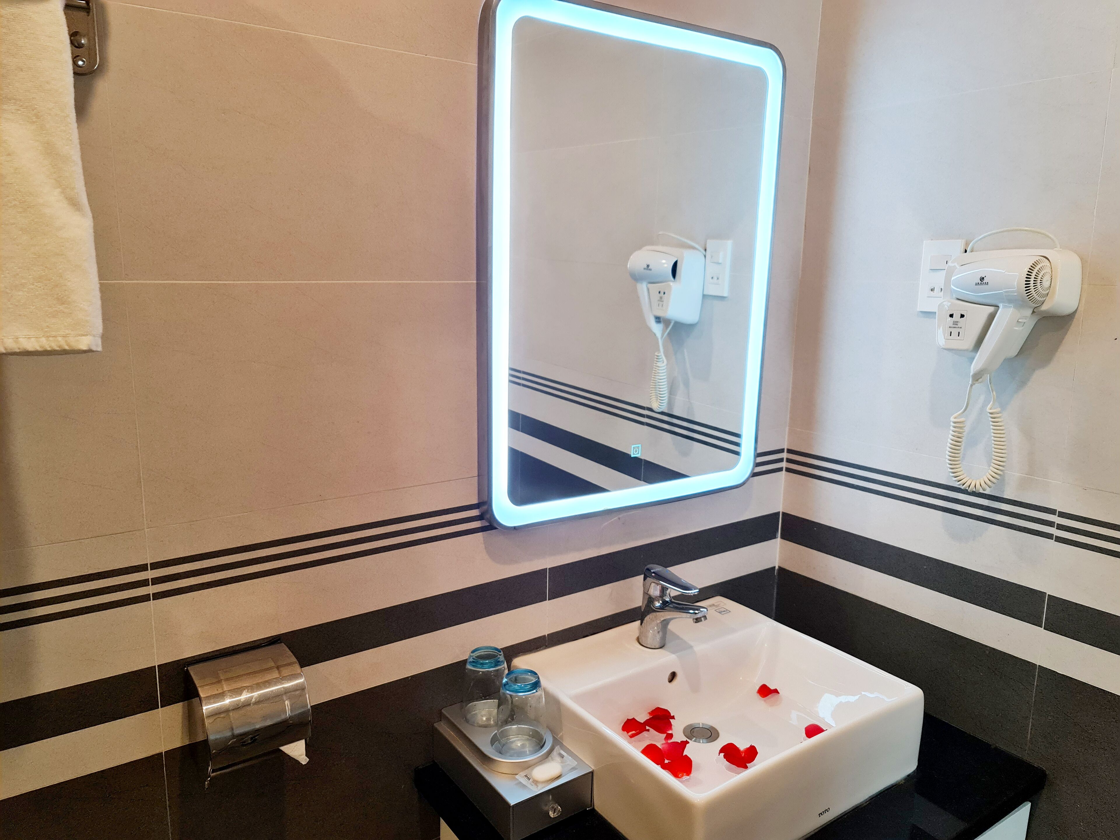 A bathroom with a white sink, a mirror with LED lighting, a hairdryer, and a towel rack.
