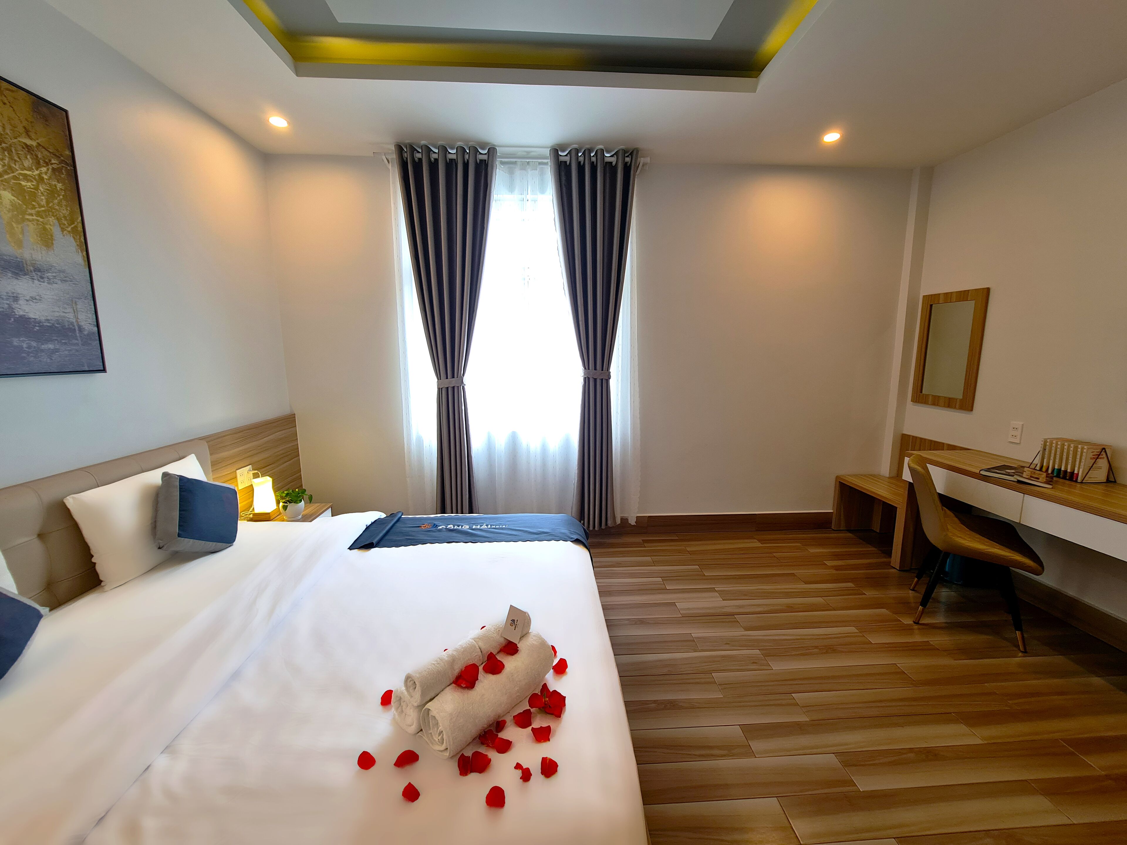 Una habitación de hotel con cama, escritorio, silla, ventana con cortinas y una lámpara en el techo.