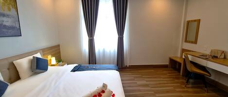 Una habitación de hotel con cama, escritorio, silla, ventana con cortinas y una lámpara en el techo.