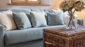 A grey sofa with patterned cushions, a wicker coffee table, and a vase with flowers.