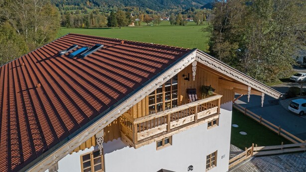 A chalet with a sloped roof, wooden balcony, and a view of a mountainous landscape.