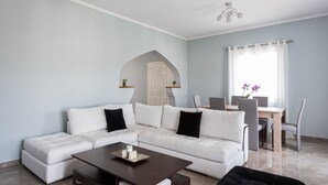A modern living room with a sectional sofa, a coffee table, and a dining area with a table and chairs. - Old Port Spetses Mansion (Spetses)