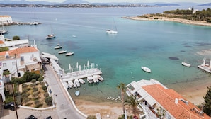 A coastal marina with boats docked, a sandy beach, and buildings with red-tiled roofs. - Old Port Spetses Mansion (Spetses)
