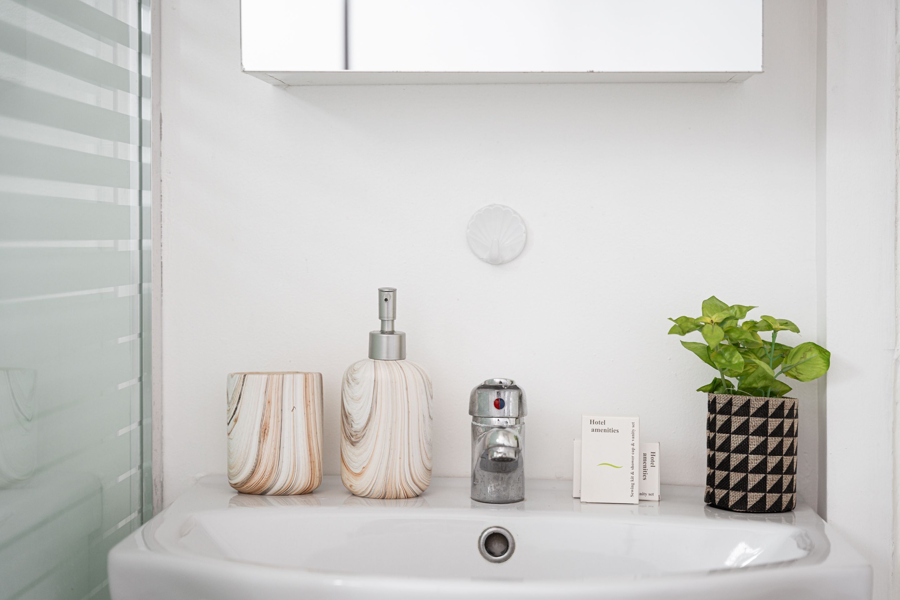 A bathroom sink with a marble-like container, a metallic soap dispenser, a small potted plant, and a white card.