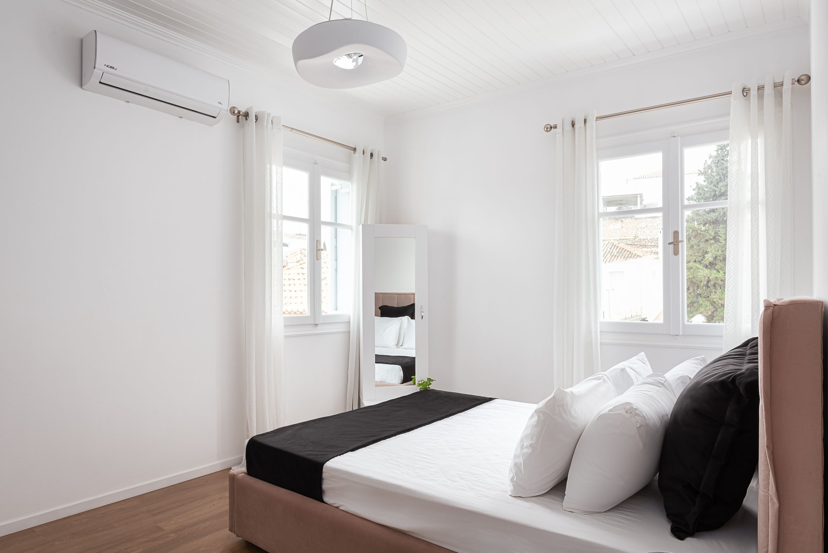 Une chambre à coucher avec un lit, des rideaux blancs, une fenêtre et un appareil de climatisation.