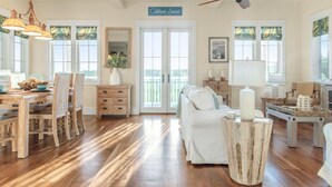 A spacious living room with hardwood floors, a dining area with a wooden table and chairs, a ceiling fan, and large windows with curtains. - Gulf Views-Resort Style Community! (Santa Rosa Beach)