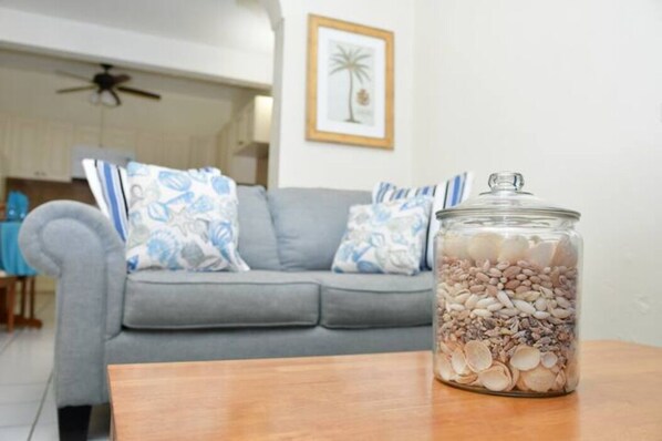 Un salon avec un canapé gris, des coussins à motifs et un bocal en verre rempli de différentes sortes de céréales, posé sur une table en bois.