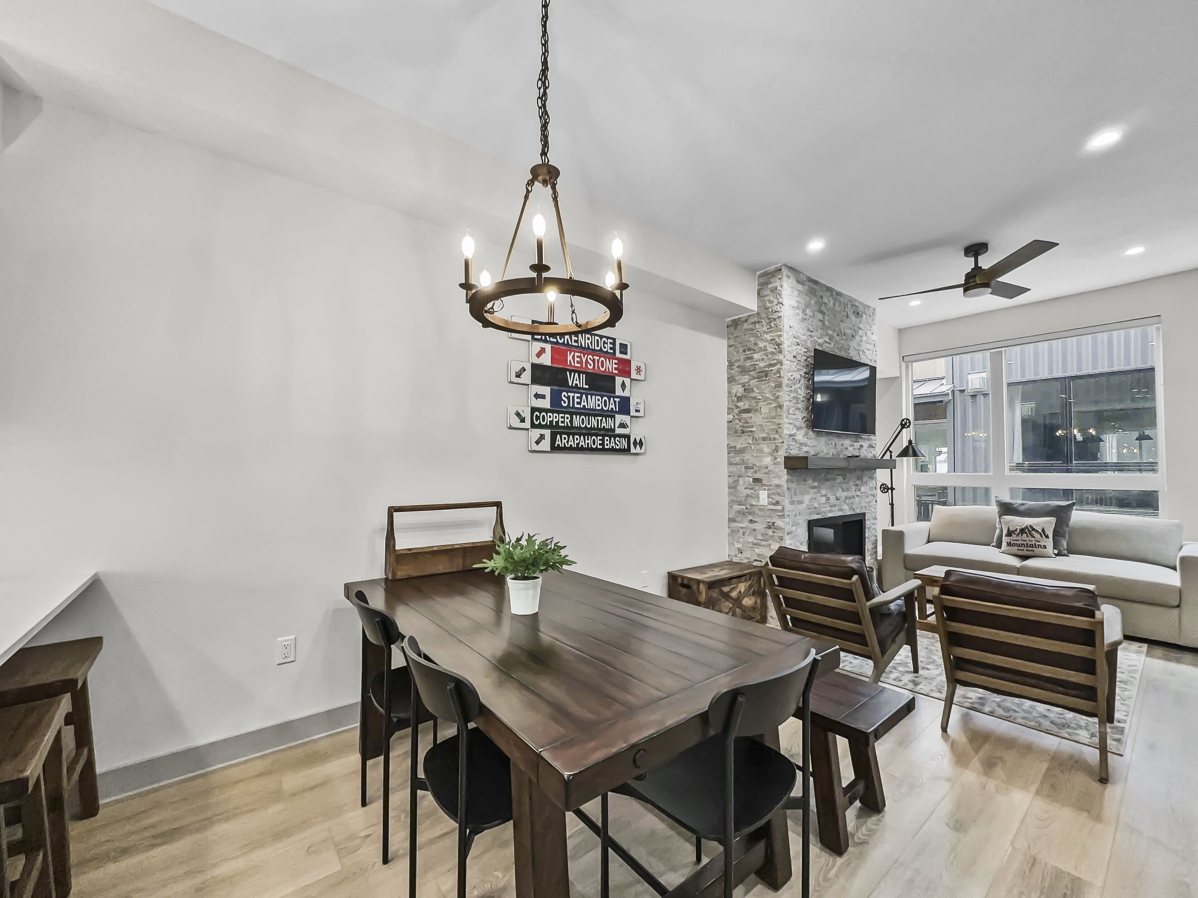 A modern dining area with a wooden table and chairs, a chandelier, and a stone accent wall.