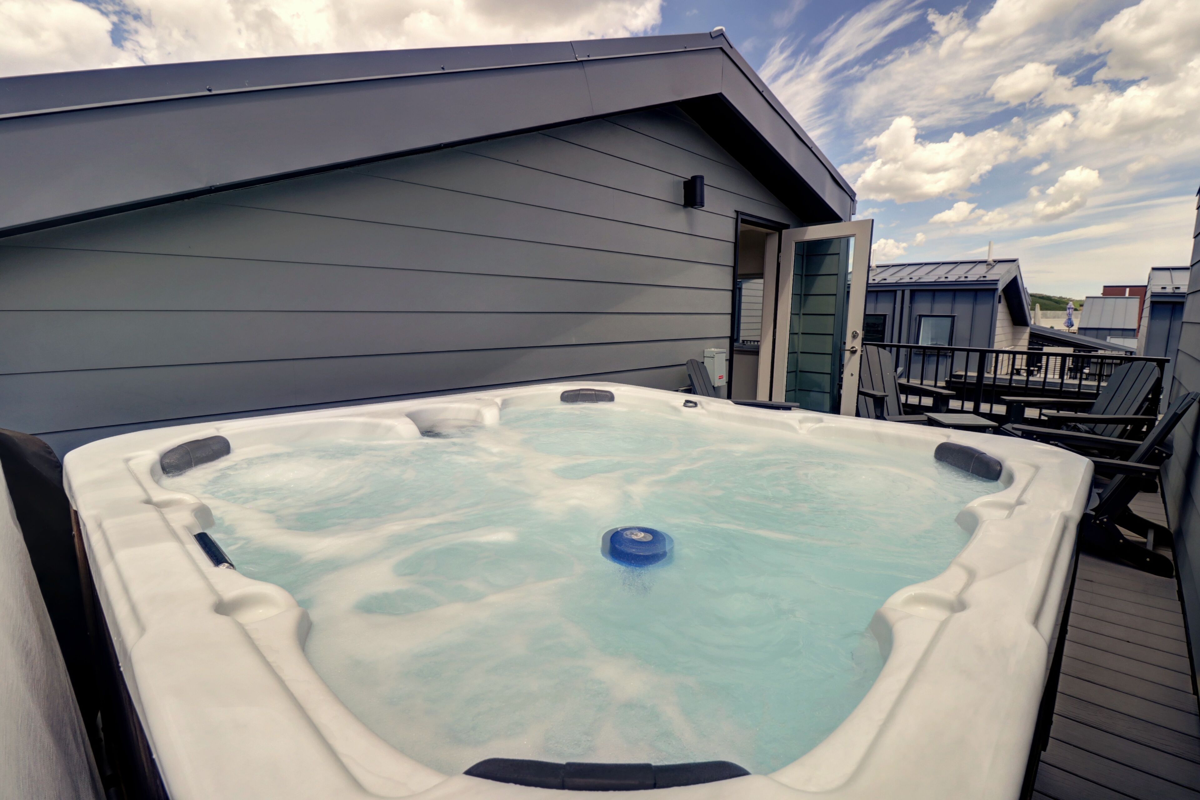 Un jacuzzi en una terraza de madera con vista a una casa y un cielo nublado.
