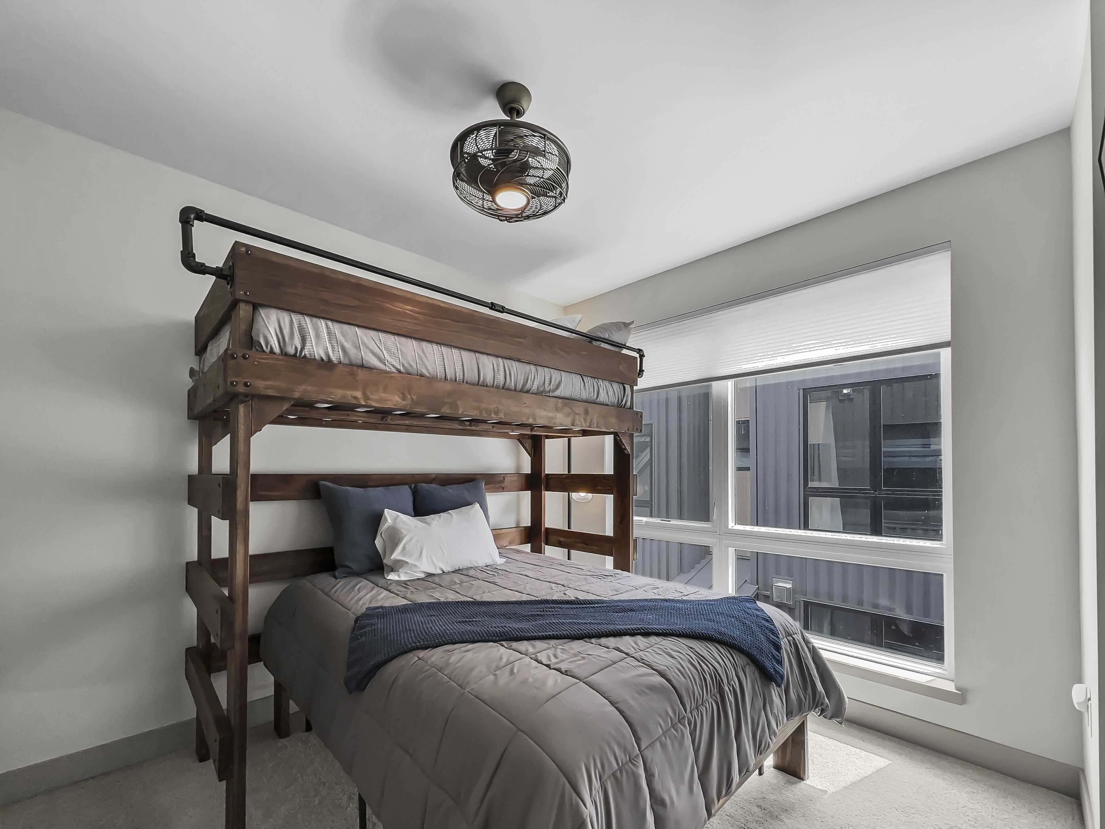 A bedroom with a bunk bed, a large window, and a ceiling fan.