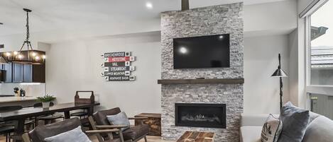 A modern living room with a stone fireplace, a flat-screen TV, and a ceiling fan.
